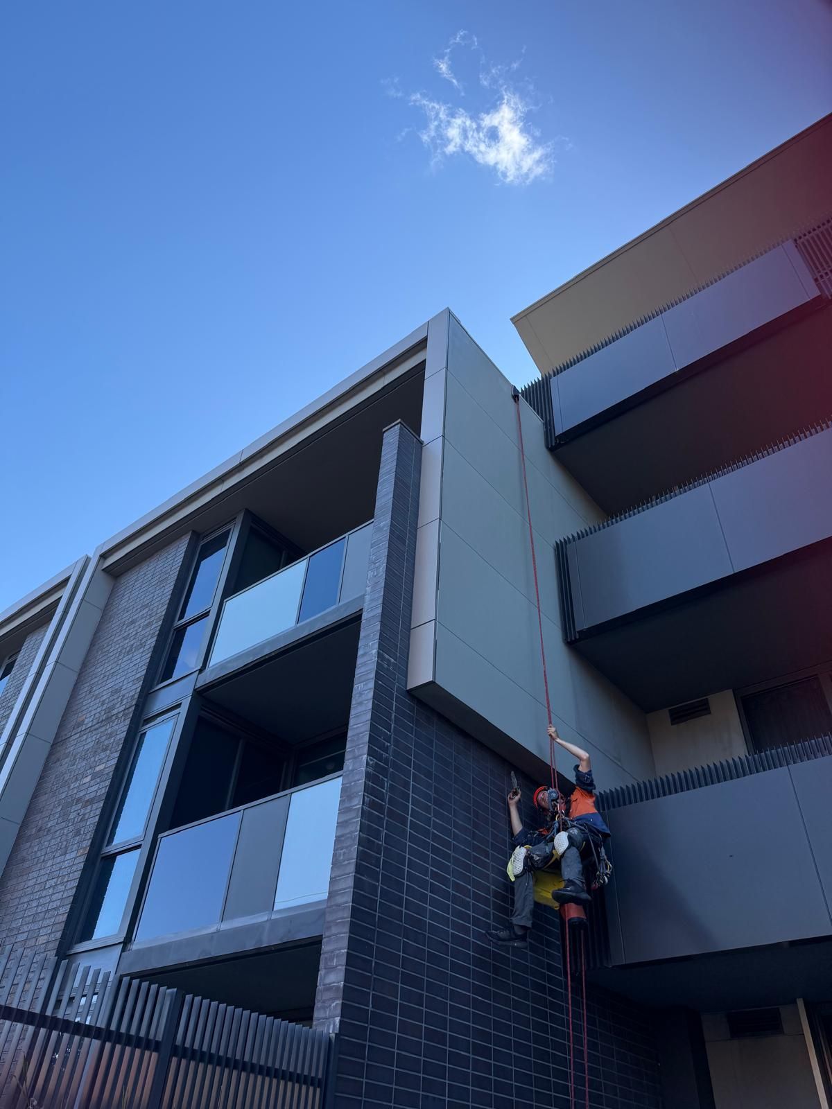 Technician on ropes repainting apartment facade after repairs, Camberwell