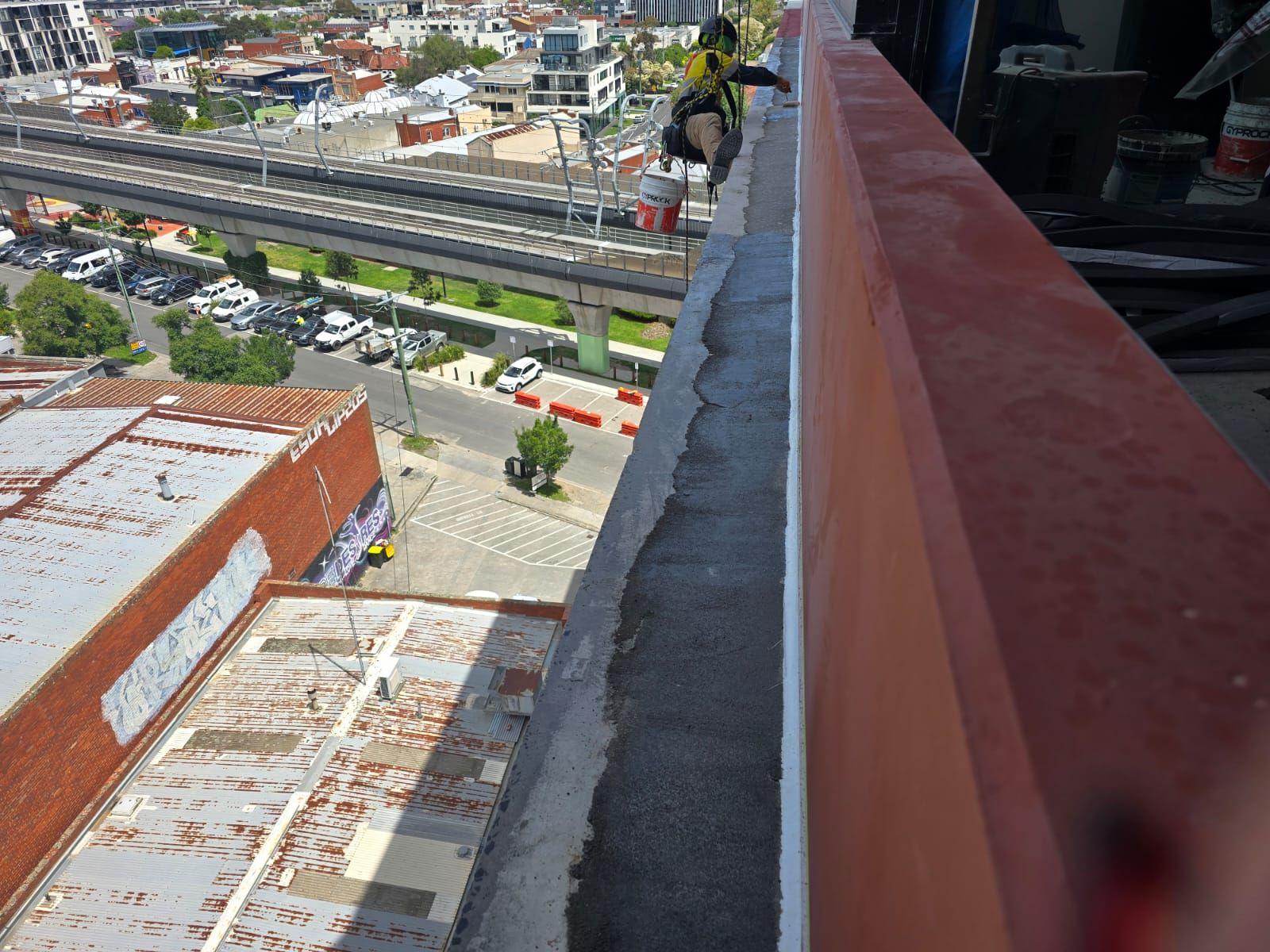 Rope access technician working on parapet high above the street, facade remediation Melbourne